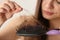 Woman untangling her hair from brush on light background