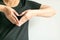 A woman use hands display love symbol by splice fingertips together to be heart shape at front of left chest