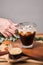 Woman used hand take cold iced black brew coffee in a glass with pieces of ice on a wooden table, natural light, fresh summer