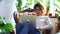 Woman uses laptop and sits in chair on background of green plants at home spbd.