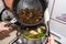 The woman uses a silicone spatula to add fried mushrooms and onion from frying pan to the vegetable soup decoction.