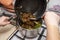 The woman uses a silicone spatula to add fried mushrooms and onion from frying pan to the vegetable soup decoction.