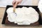 The woman uses a spoon to form the mixed curd and whipped cream on a baked cocoa cake on a baking sheet.