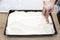 The woman uses a spoon to form the mixed curd and whipped cream on a baked cocoa cake on a baking sheet.