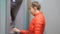 Woman using cash machine. Attractive young female in red bubble jacket inserting credit card into ATM and entering pin