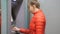 Woman using cash machine. Attractive young female in red bubble jacket inserting credit card into ATM. Woman smiling