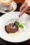 Woman using fork cutting chocolate fondant cake with fudge and cup of cappuccino coffee at restaurant