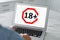 Woman using laptop with age limit sign 18+ years indoors, closeup