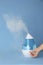 Woman using modern air humidifier on blue background, closeup