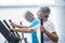 Woman using a precor at the gym - active senior with his man at the background - couple of pensioners doing exercises together