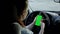 A woman using a smartphone with a green screen in her hand driving a car. Chroma key.