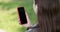 Woman using smartphone relaxes on the bench in beautiful green park. Young millennial woman making gestures on phone