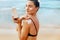 Woman using sunscreen on the shoulder holding sun cream bottle on the beach