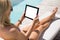 Woman using tablet computer while sitting in deck chair by the pool