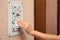 Woman using tissue paper to press elevator call button full of microbes, closeup