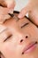 Woman using tweezers on patient eyebrow