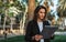 Woman using wireless earphones selects music holding laptop computer while relaxing Park in Barcelona, successful girl manager