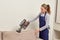 A woman vacuums the dust from the sofa cushion with a cleaning vacuum cleaner.