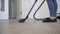 A woman vacuums the floor in the living room with a modern vacuum cleaner