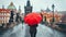 Woman with a vibrant red umbrella crossing the historic charles bridge in picturesque prague city