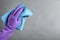 Woman in violet rubber gloves with microfiber cloth on light grey background, closeup. Space for text