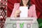 Woman voter in a smart pink jacket lowers the ballot in a transparent ballot box against the background of the national flag of