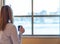 Woman waking up and looking out hotel window with coffee in hand