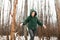 Woman walk in winter forest among bare trees looking down. Person in warm outfit from eco fur jacket relax in snow park.