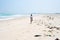 Woman walking alone on tropical beach with rubbish trash plastic on sand. Waving ocean desert beach pollution problem in the sea.