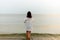 Woman walking along beach and sea sunset background.Loneliness and sadness concept.Empty place for text.Back view