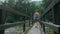 Woman Walking Along Suspension Bridge Alone in Picturesque Green Forest Setting.