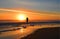 Woman walking on the beach at sunrise.