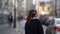 Woman is walking in city at cold autumn day, listening to music by headphones, rear view in movement