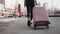 Woman walking on a city street and rolling a wheeled suitcase behind her close up, view from behind. Concept of travel