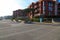 A woman walking a dog on a long bike path at the beach surrounded by red apartment buildings and lush green trees and plants