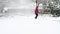 Woman walking down a snow-covered driveway with a snow shovel in blowing snow, snowing in a residential front yard garden