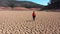 Woman walking through dry areas with cracked drought land texture. Concept of climate change, global warming and lack of