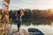 Woman walking on lake pier by boat admiring autumn landscape holding leaves. Fall season activities