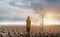 Woman walking in an open expansive field at the tree is dried on cracked soil