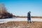 Woman walking pug dog in snowy winter park by frozen lake holding leash. Puppy wearing harness