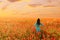 Woman walking in red poppies meadow at sunset.