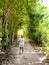 Woman walking in rustic pathway between trees on a sunny day