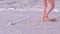 Woman walking on sand beach with foaming waves of the ocean.