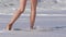 Woman walking on sand beach leaving footprints in the sand. Foaming waves