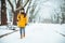 woman walking by snowed city park with thinking face with coffee cup. warm up cold day