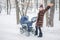 Woman walking with stroller in forest at winter.