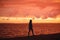 Woman walks alone on the beach and looks at the colorful sunset after the rain. Beautiful scenery, focus on waves