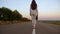 Woman walks along asphalt outside city wearing pants and jacket and white high-heeled shoes, businesswoman carries black