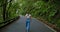 Woman walks along an asphalt road in a dense forest. Overgrown trees in laurel tree forest or jungle, Anaga National