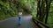 Woman walks along an asphalt road in a dense forest. Overgrown trees in laurel tree forest or jungle, Anaga National